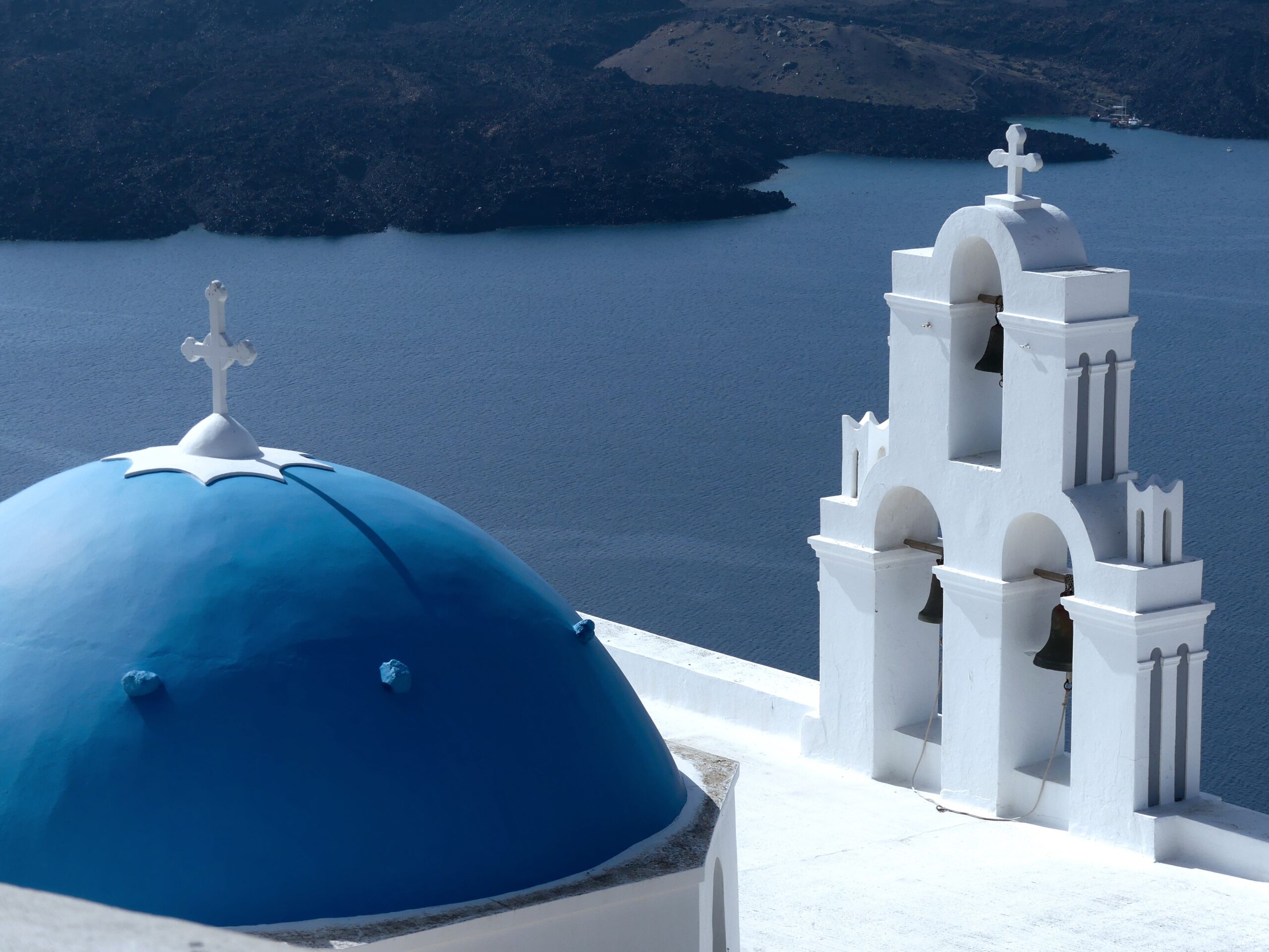 Beautiful view of Santorini's iconic blue-domed church with a bell tower, overlooking the calm Aegean Sea.
